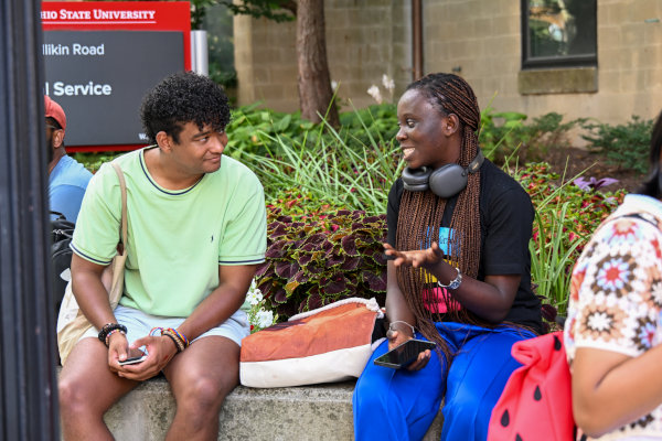Two people sit on a stone bench outdoors, talking.